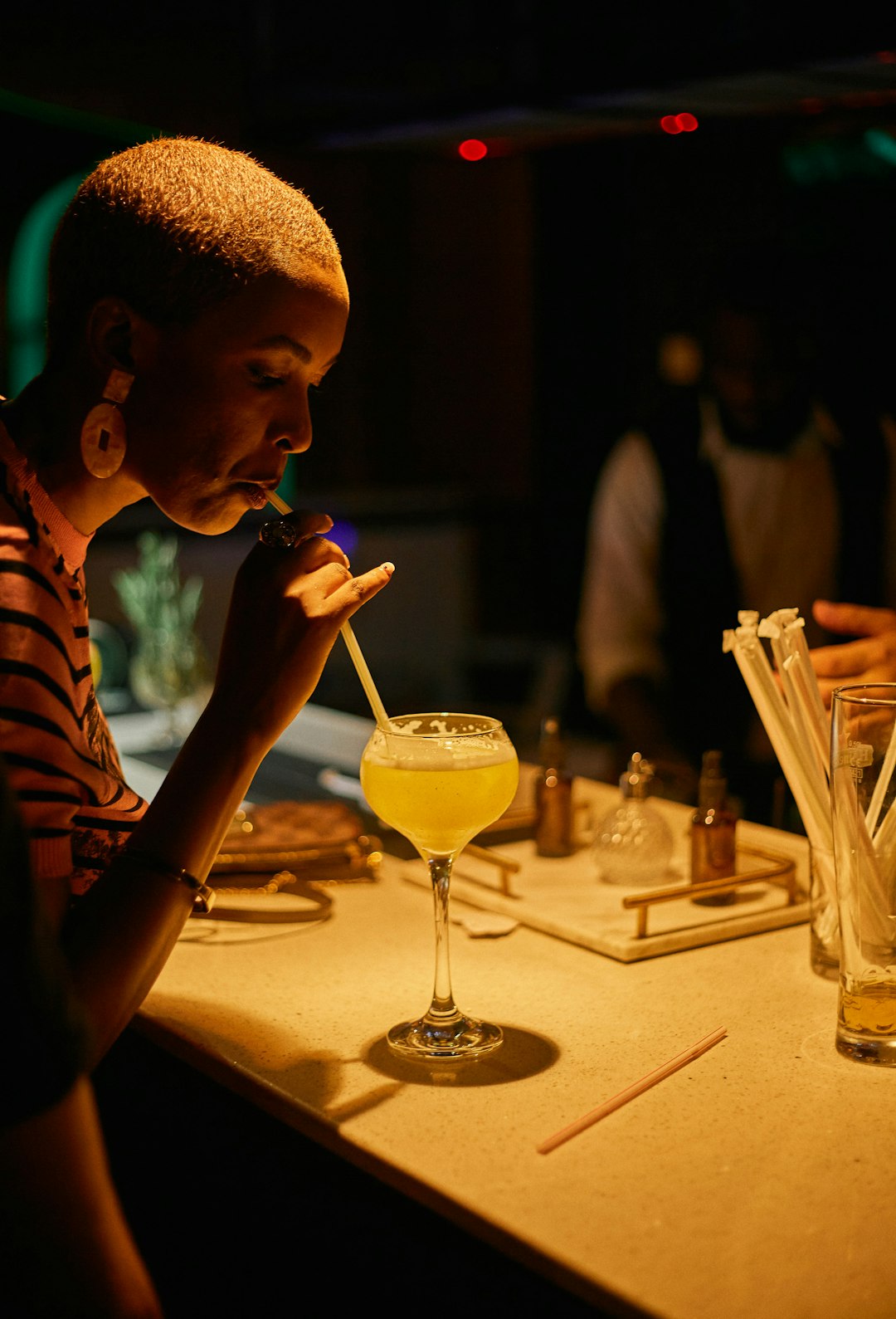 Woman drinks a yellow cocktail at a bar.